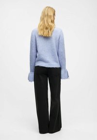 Hellblauer, strukturierter Pullover mit lockeren Ärmeln und gerippten Bündchen, kombiniert mit hoch taillierten, schwarzen, weit geschnittenen Jeans, von hinten betrachtet.