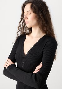Black ribbed long-sleeve top featuring a V-neck and buttoned front detail. The fabric has a soft texture with a fitted silhouette.