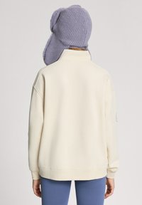 Kremowy, oversize'owy sweter z prążkowanymi mankietami, połączony z lawendową dzianinową czapką z uszami i miękką teksturą.