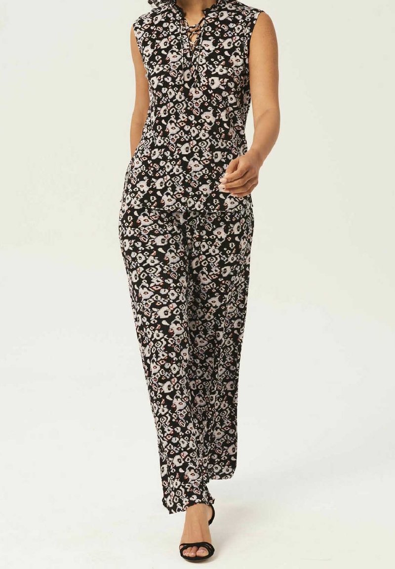 Blommig jumpsuit med svart bas, korta ärmar och snörning i halsen. Flödande, lätt material och vida ben för komfort.