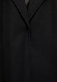 Čierny vlnený kabát s klopovým golierom, čistými líniami a jemnou textúrou. Navrhnutý s minimálnym prešívaním a prispôsobeným strihom.