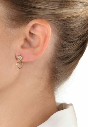 Pendientes en forma de corazón en tono dorado que destacan por su parte superior brillante y un diseño de corazón colgante. Cristales claros acentúan la sección superior.
