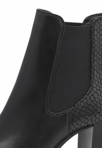 Bottine noire en cuir lisse, avec panneau latéral élastique et accent texturé effet peau de serpent. Talon carré et design élégant.