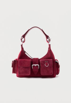 Small burgundy suede handbag with a short handle, front buckle, two front flap pockets, and side pockets with buckles.