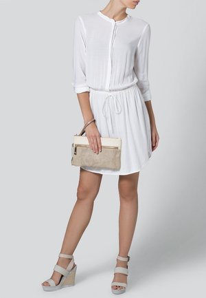 Valkoinen, napitettava mekko, jossa pitkät hihat ja nyörityskaistale vyötäröllä. Yhdistetty beigen sävyiseen tekstuuriin ja vaaleanharmaisiin kiilakorkosandaaleihin.