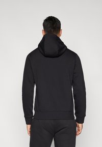 Fekete kapucnis pulóver puha textúrával, bordázott mandzsettákkal és szegéllyel. A hátulján hangsúlyos kapucni és egyszerű kialakítás található.