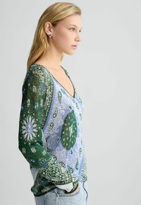 Lange mouwen blouse in lichtblauw en groene paisleyprint. Heeft een V-hals, gemusterde mouwen en een ontspannen pasvorm. Gemaakt van zachte stof.