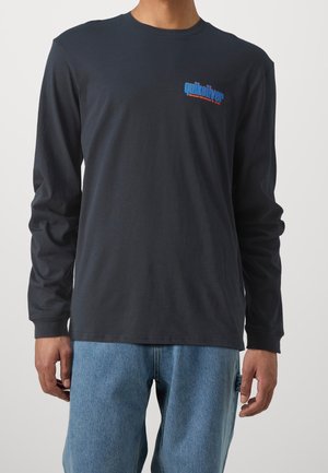 Black long-sleeve shirt made of cotton, featuring a blue and red logo on the left chest. Worn with light blue denim jeans.