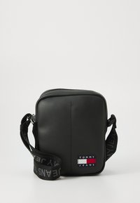 Svart syntetisk crossover-veske med firkantet fasong, justerbar logo-reim og liten brodert "TOMMY JEANS" lapp på fronten.