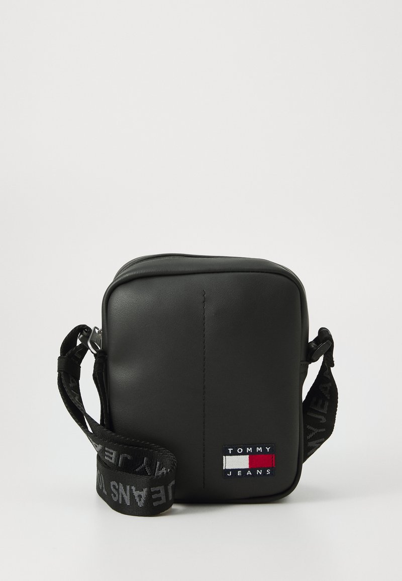 Sort syntetisk crossbody taske med firkantet form, justerbar logo skulderrem og lille broderet "TOMMY JEANS" patch foran.