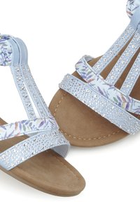 Helle blaue Sandalen mit einem T-Riemen-Design, das mit Kristallakzenten, floral gemustertem Stoff und einer weichen, strukturierten braunen Außensohle versehen ist.
