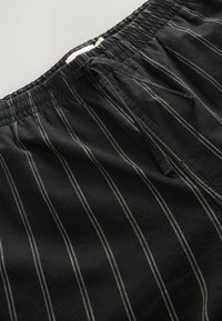 Schwarze Hose mit weißen vertikalen Streifen, ausgestattet mit einem elastischen Bund und Kordelzug. Der Stoff wirkt weich mit einer glatten Textur.