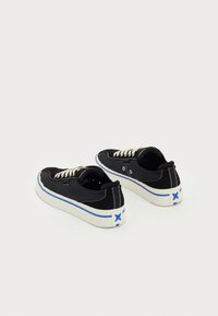 Black canvas sneakers with white laces, a rubber sole, and a blue star accent on the heel. Features contrasting white stitching and eyelets.