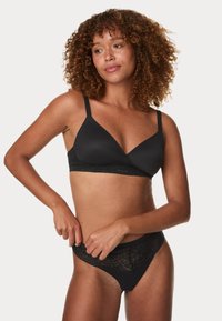 Soutien-gorge noir en tissu lisse avec une finition en dentelle. Dispose de bretelles réglables et d'une forme triangulaire. String noir en dentelle assorti avec une ceinture décorative.