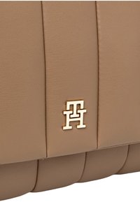 Borsa a mano in pelle beige con superficie testurizzata, pieghe orizzontali e dettaglio logo metallico dorato.