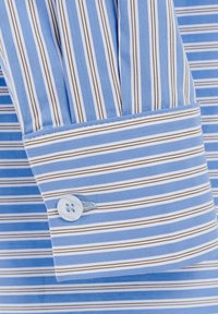Polsino a righe in azzurro chiaro e bianco con righe marroni. Presenta un singolo bottone blu e una texture del tessuto liscia.