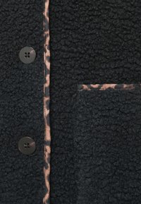 Μαύρο φλις παλτό με υφή, που διαθέτει λεοπάρ σχέδιο στις βάσεις των κουμπιών και της τσέπης, καθώς και μαύρα κουμπιά.