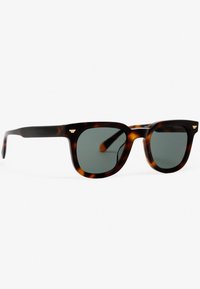 Gafas de sol de carey marrón con lentes verdes. Montura cuadrada con un acabado suave. Pequeños acentos dorados en las patillas.