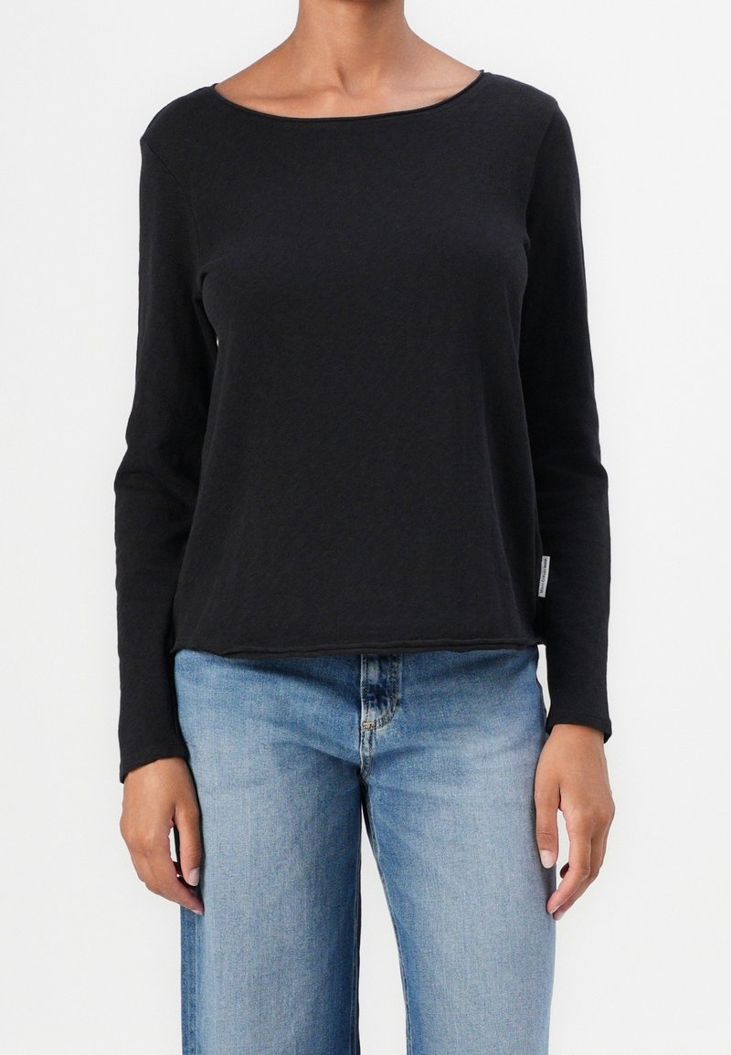 Svart långärmad tröja med rund halsringning, tillverkad av mjukt tyg, med en avslappnad passform och rak nederkant, i kombination med ljusblå jeans.