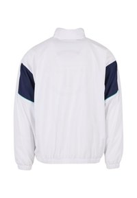 Fehér széldzseki sötétkék vállbetétekkel. Magas gallérral, elasztikus mandzsettákkal és kör alakú perforált logóval a hátsó részén.