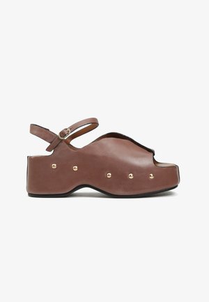 Brązowy skórzany sandał na platformie z odkrytym palcem, złotymi nitami wzdłuż podeszwy i regulowanym paskiem wokół kostki z małą klamrą.