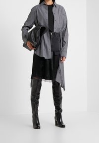 Randig skjorta i svart och vitt med knappar, över en svart topp, kombinerad med en svart satin kjol och knähöga svarta läderstövlar.