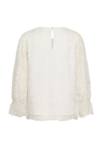 Haut en dentelle blanche avec un col rond, des manches longues à volants aux poignets et un détail d'ouverture en forme de clé dans le dos. Motif floral texturé sur l'ensemble.