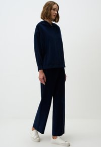 Pull bleu marine à capuche, avec des manches longues et une coupe décontractée, associé à un pantalon large assorti et des baskets blanches.