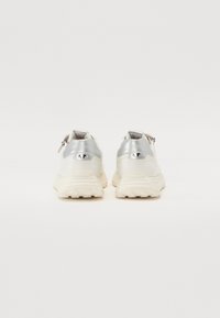 Fehér bőr sneaker ezüst metallikus részletekkel. Vastag, texturált talp és cipzárral ellátott hátsó rész a könnyű felvétel érdekében.