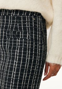 Svart och vit tweedbyxa med ett strukturerat mönster med vertikala ränder, en bakficka och en märkesdetalj nära midjan.