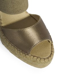 Espadrille à bout ouvert avec une tige en bronze métallique, une semelle en jute et une bride de cheville en tissu texturé. Semelle intérieure plate de couleur naturelle.