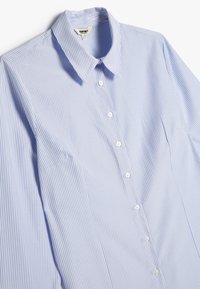 Camisa de botones a rayas azul claro hecha de algodón. Presenta un cuello clásico y botones blancos a lo largo de la tapeta. Textura suave y lisa.