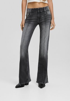 Flared black denim jeans with a faded finish, featuring front pockets, belt loops, and contrasting stitching. Paired with pointed black shoes.