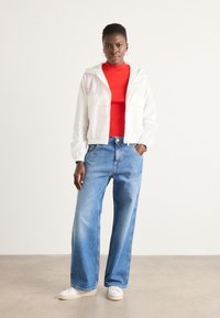 White cropped jacket with drawstring hood, red fitted shirt, light blue wide-leg jeans, and white sneakers. Textured fabric, casual style.