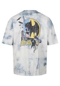 Camiseta de algodón con un patrón de teñido anudado azul, una gran gráfica de Batman y murciélagos, con el texto "BATMAN" en amarillo en la parte posterior.