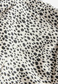 Tejido negro y crema con un patrón de estampado de leopardo disperso, con manchas de diferentes tamaños y texturas. Superficie suave con un ligero brillo.