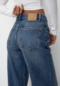 Högmidjade blå denimjeans med en blekt finish, med en läderetikett på midjebandet och standardbakfickor.