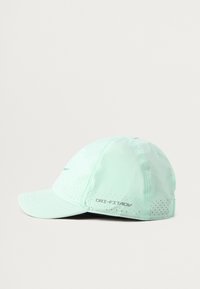 Minti zaļa cepure ar izliekto malu, izgatavota no viegla materiāla, ar perforeitiem elementiem ventilācijai un "DRI-FIT ADV" logo malā.