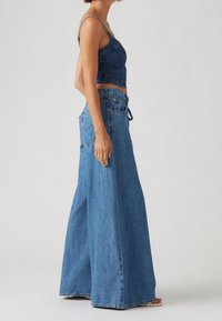 Denim crop top met dunne bandjes, gecombineerd met wijde, hooggetailleerde jeans. Beide items hebben een diepblauwe wassing en een minimalistisch ontwerp.