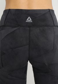 Černé sportovní legíny s texturovanou tkaninou a geometrickým vzorem, s zesíleným švem a malým logem Reebok na pásu.
