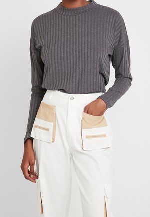 Osoba ubrana w szary prążkowany długi rękaw włożony do białych spodni z dużymi beżowymi i białymi kieszeniami naszywanymi.