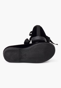 Zapato de terciopelo negro con suela de goma, que presenta una forma redondeada y cordones de cinta. La suela tiene patrones de agarre texturizados y detalles de marca.