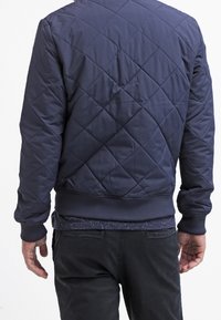 Námořnická prošívaná bomber bunda vyrobená z hladkého nylonu s žebrovanými manžetami a lemem, s klasickým kulatým výstřihem a elegantní siluetou.