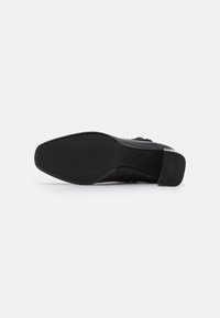Zapato de cuero negro con punta cuadrada y un tacón bajo y grueso. Textura suave con una suela sólida y un diseño minimalista.