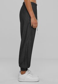 Grey joggers with an elastic waistband, drawstring, and tapered cuffs, paired with white sneakers. The fabric appears textured and lightweight.