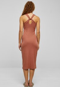 Rochie midi de culoare ruginie cu un design ajustat, având o curea la spate legată și o deschidere în formă de cheie. Materialul fin și texturat se extinde până la jumătatea gambei.
