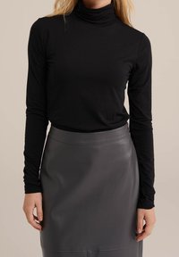 Svart långärmad polotröja i mjukt, slätt material, kombinerad med en mörkgrå, figursydd läderkjol med minimal design.