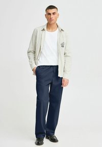 Striped light beige and white button-up shirt over a white t-shirt, paired with navy blue trousers and black shoes.