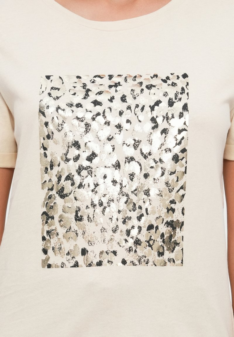 Camiseta de manga corta color crema con un diseño de estampado de leopardo en negro y dorado metálico en forma rectangular en el centro.