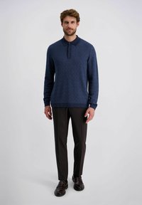 Dunkelblaues Strickpolo mit einem strukturierten Fischgrätenmuster, einer Knopfleiste mit drei Knöpfen und langen Ä sleeves, kombiniert mit enganliegenden dunklen Hosen.